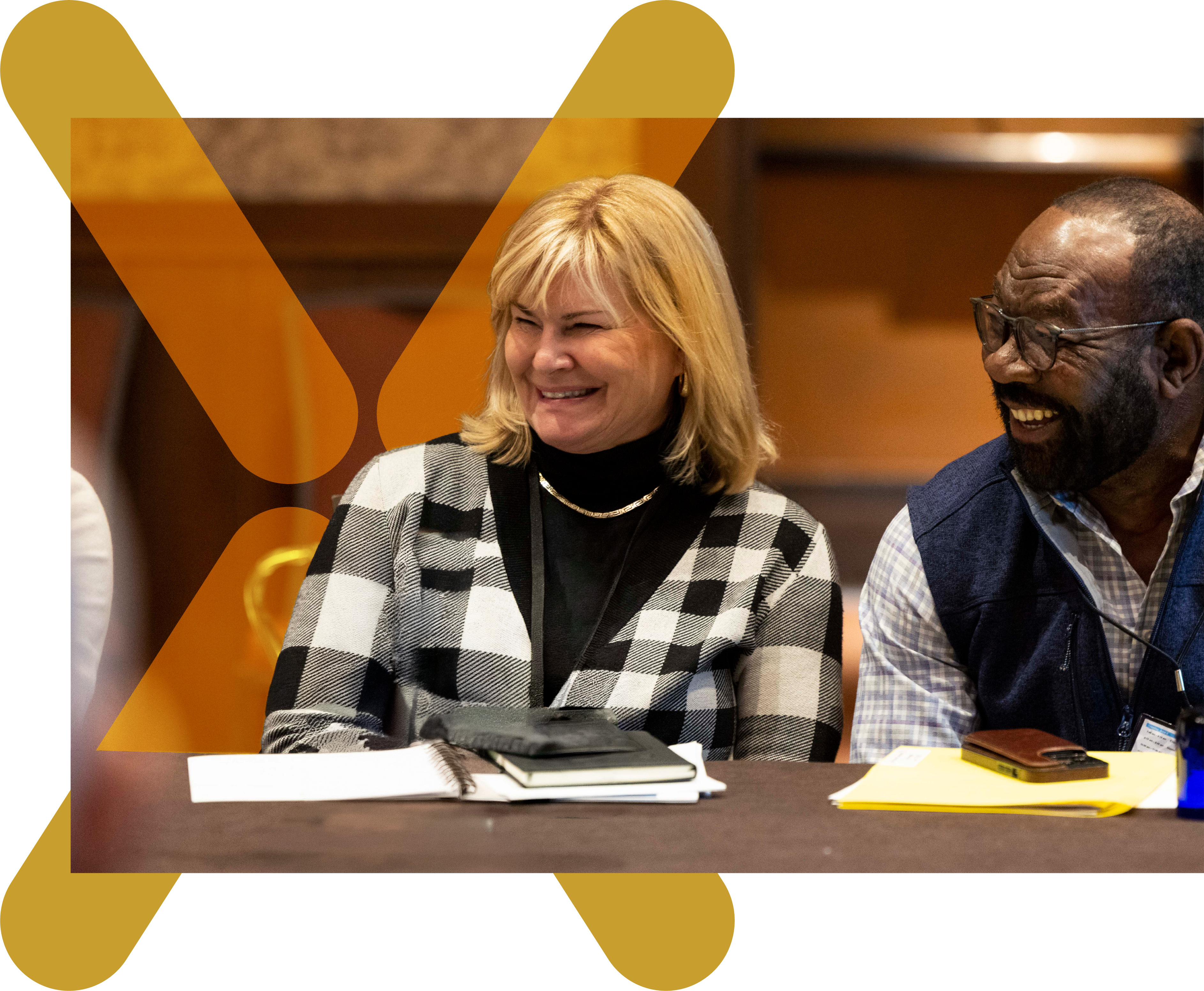Two CEO Exchange attendees laughing during a conference session, with gold X design overlay