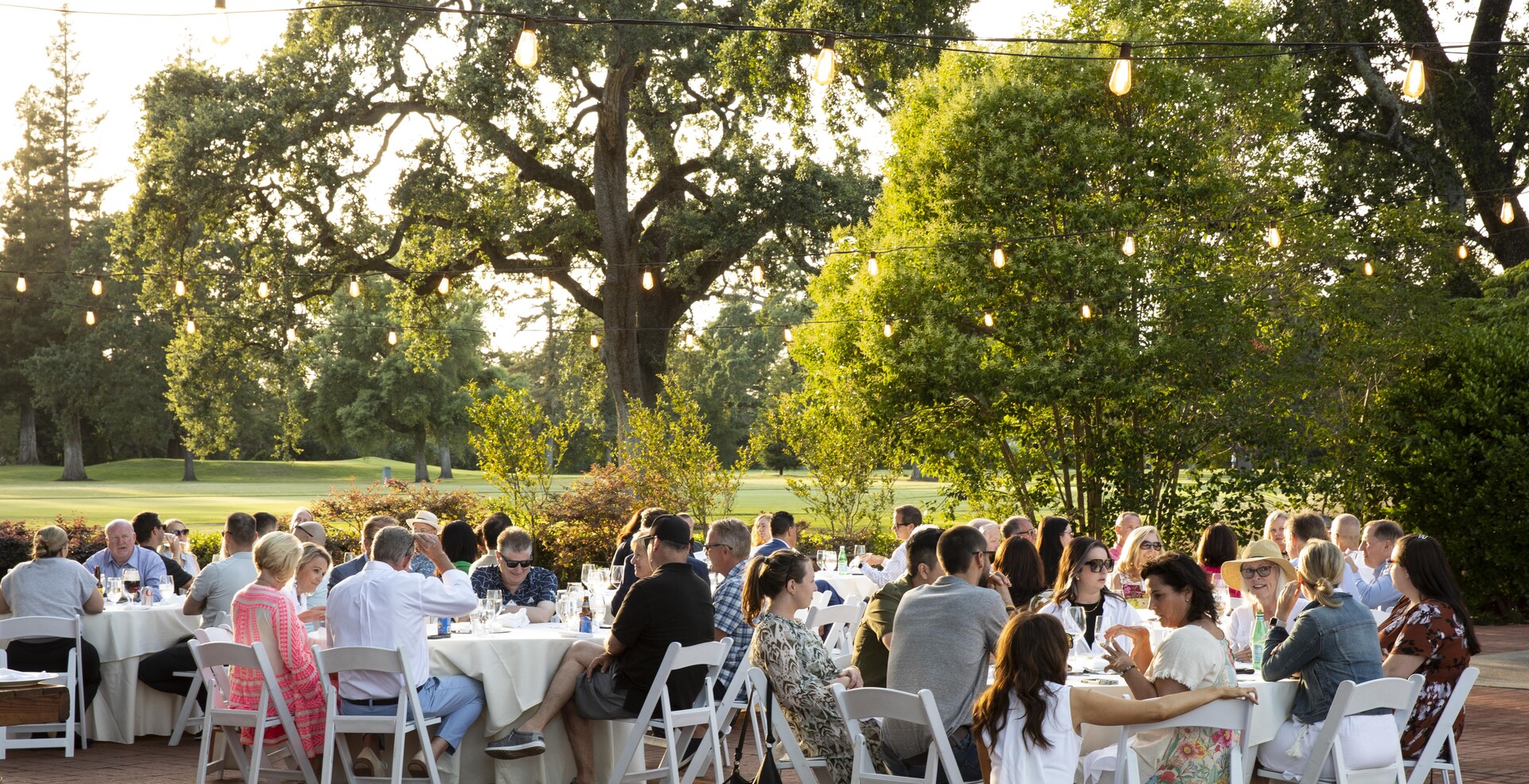 CEO Exchange attendees dining together at an outdoor evening reception under string lights