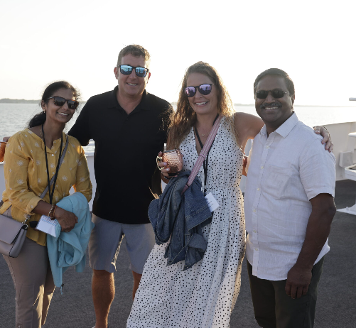 Four HealthLeaders Exchange members posing together at a waterfront sunset reception